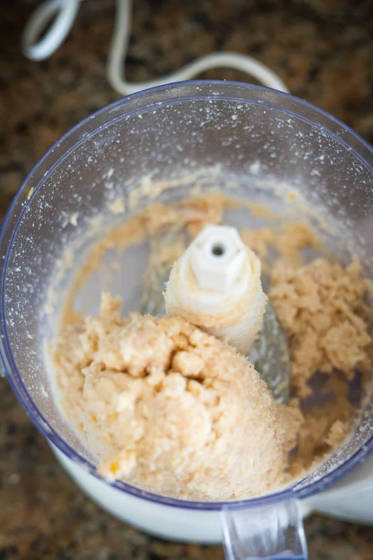 Top view of a food processor containing freshly made chicken piccata meatballs dough with a visible blade attachment, placed on a kitchen counter.