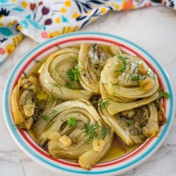 A colorful plate of braised fennel garnished with fresh dill on a marble surface.