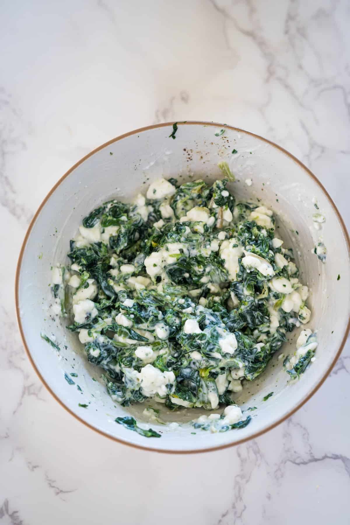 A bowl of creamy spinach and feta cheese mixture on a marble surface.
