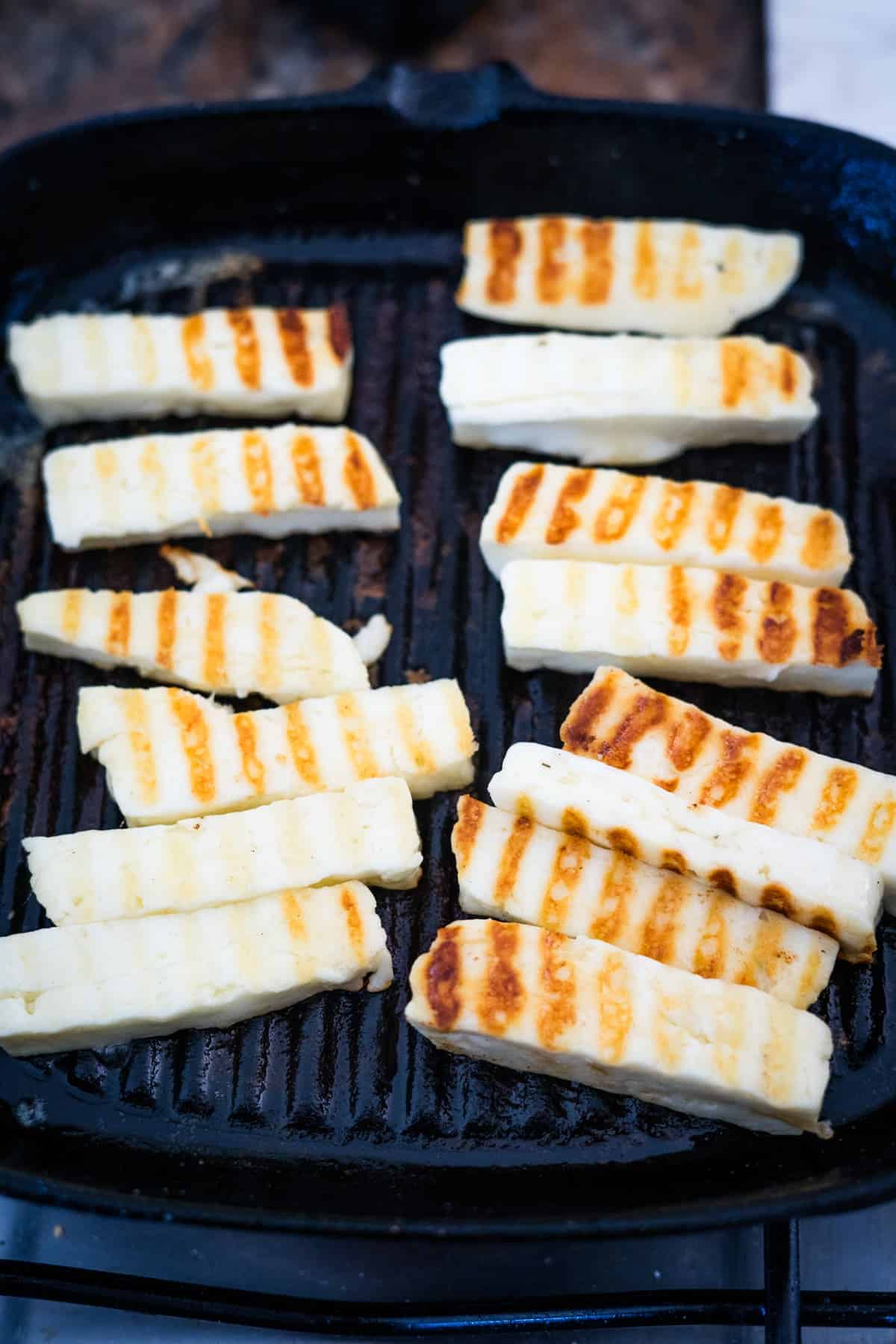 Grilled halloumi cheese slices with grill marks on a black grill pan, served with chicken salad.