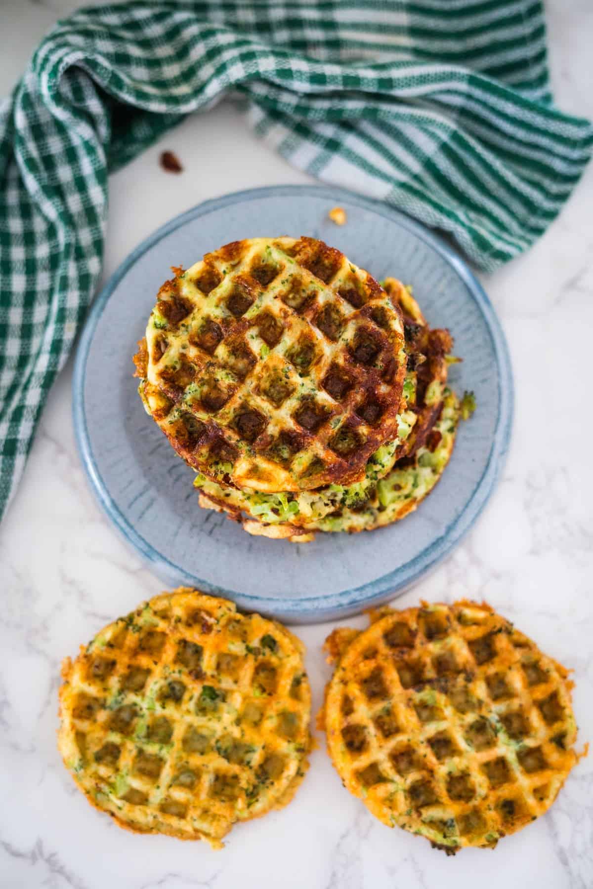 A stack of three savory broccoli cheddar waffles on a blue plate with a green striped napkin on the side.