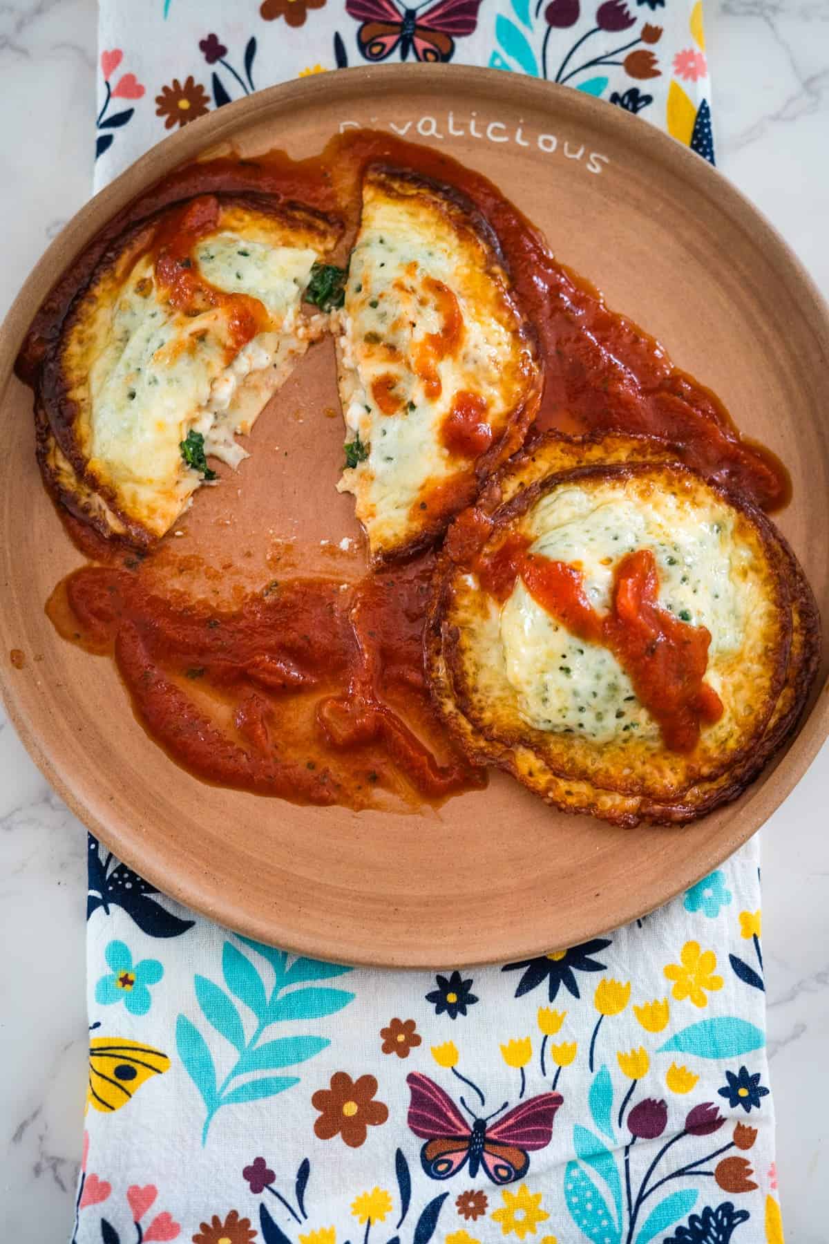 A plate with a slice missing from a keto spinach and cheese pizza, displayed on a floral napkin.