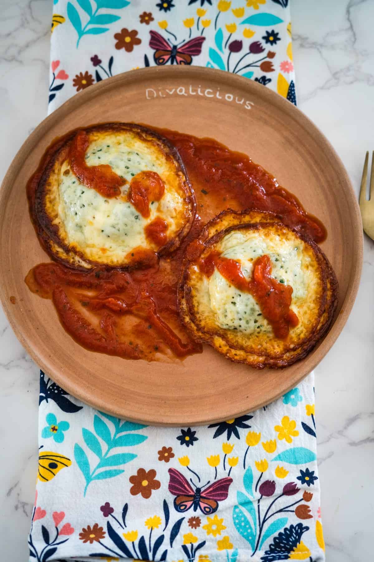 Two cheese stuffed ravioli and tomato sauce on a clay plate, placed on a floral and butterfly patterned napkin.