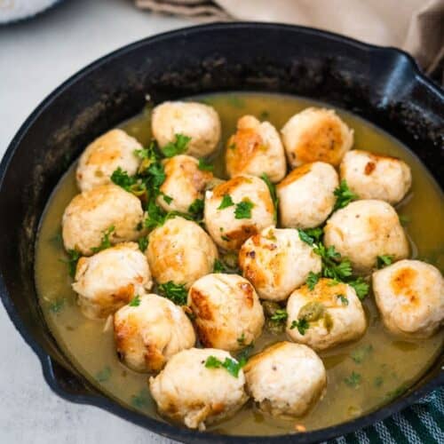 A skillet containing chicken meatballs garnished with parsley in a light broth.