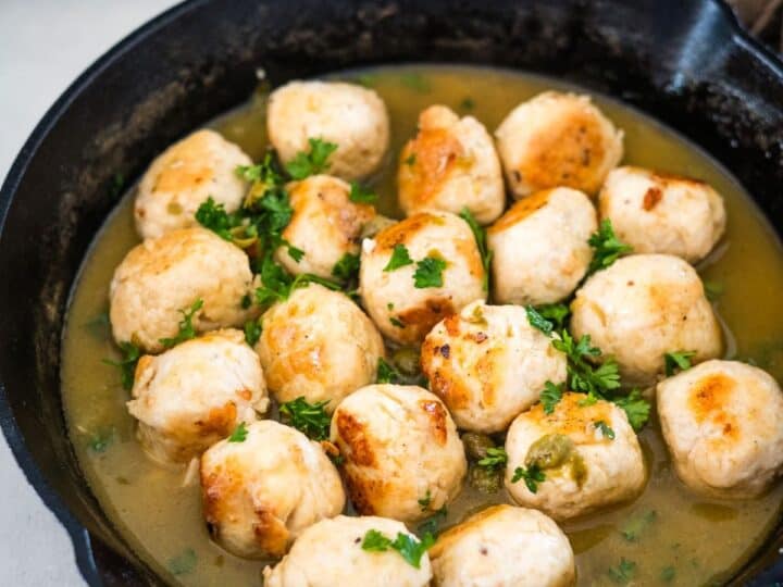 A skillet containing chicken meatballs garnished with parsley in a light broth.