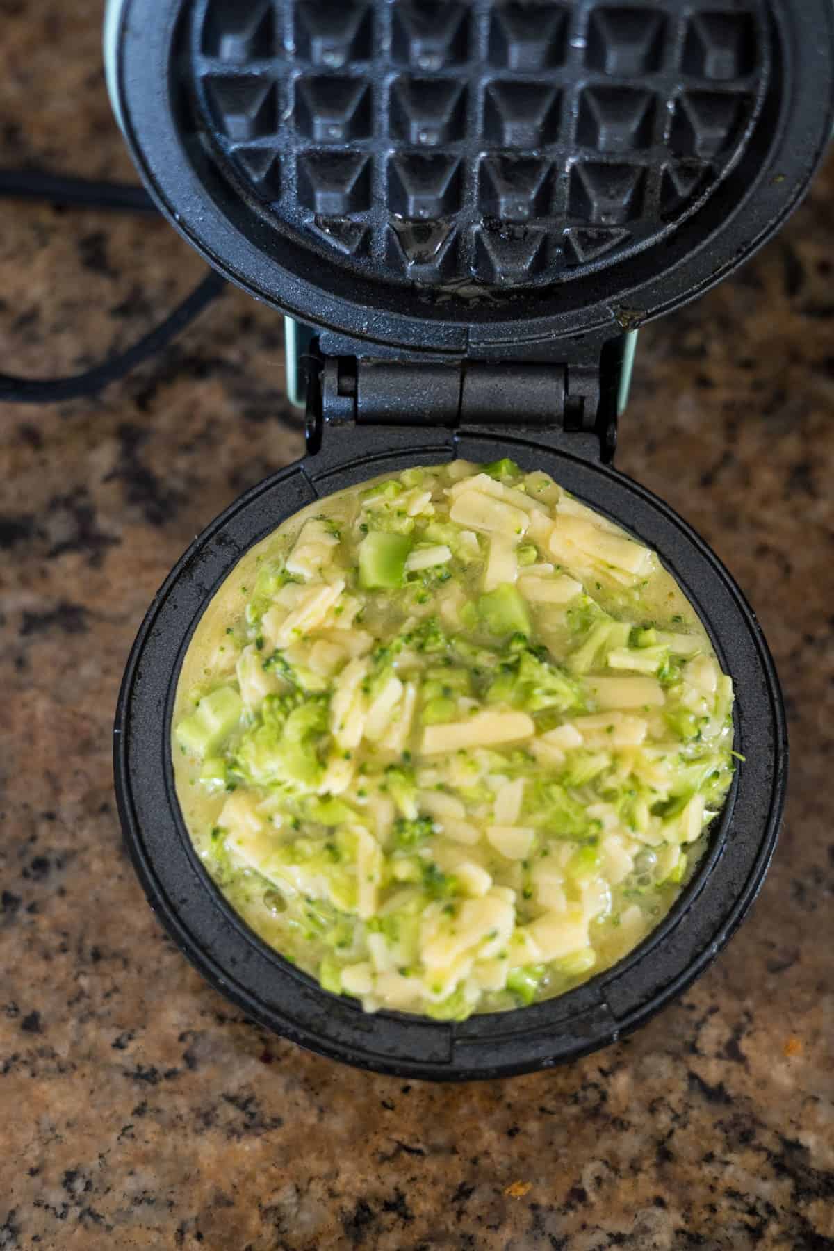 Vegetable batter with broccoli and cheddar poured into a waffle iron, ready to cook.