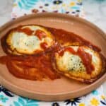 Two keto baked eggs in tomato sauce served on a ceramic plate.