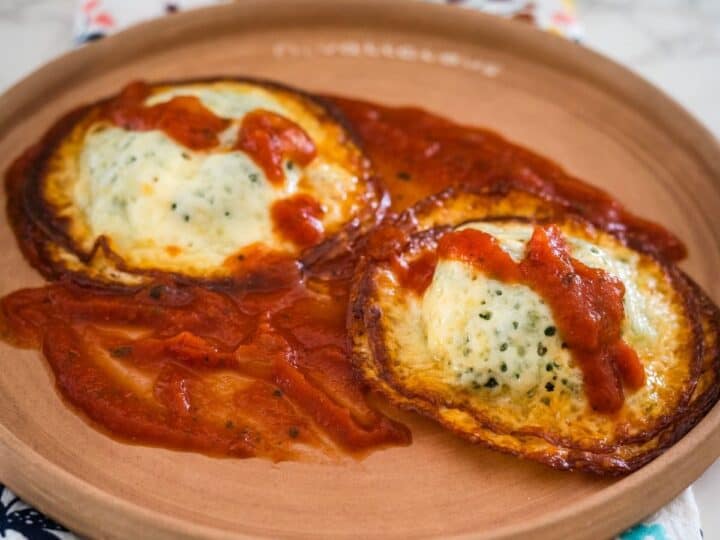 Two keto baked eggs in tomato sauce served on a ceramic plate.