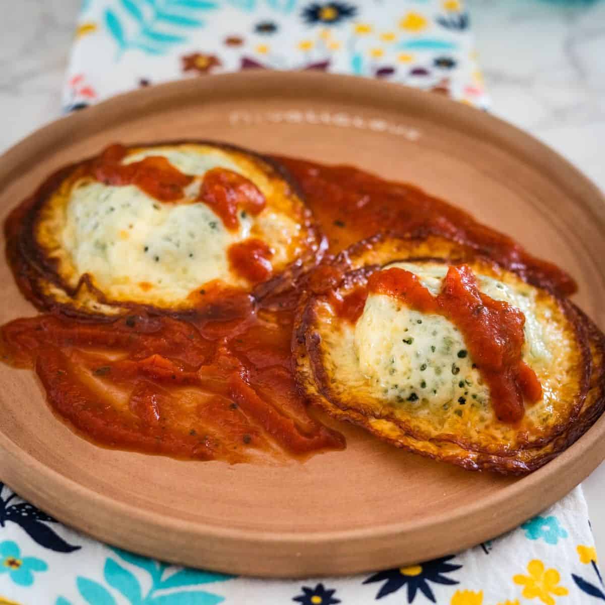 Two baked eggs in tomato sauce served on a round, clay plate with a floral napkin underneath.