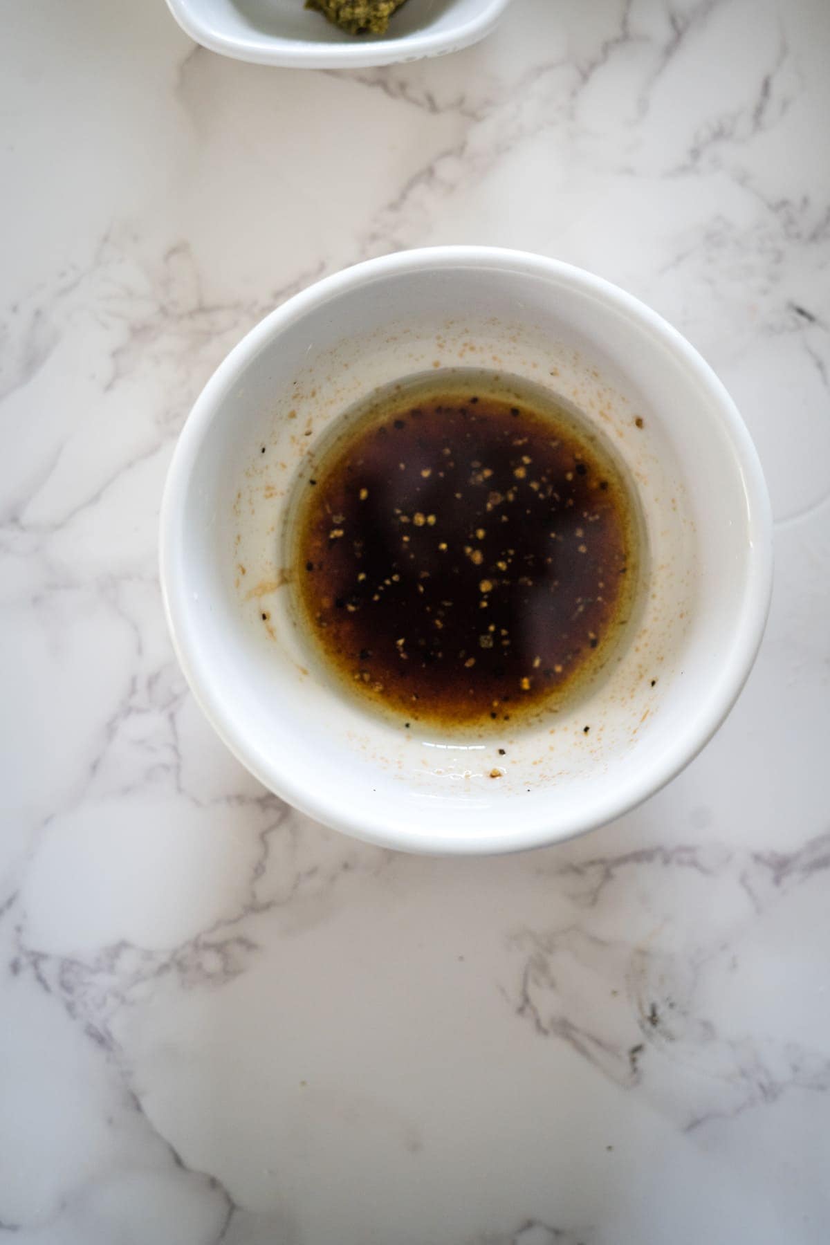 Top view of a white bowl with soy sauce on a marble surface, accompanied by another bowl with seasoning.