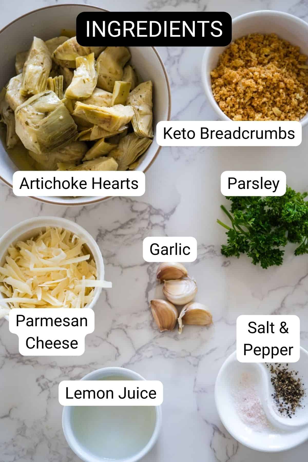 Image showing ingredients labeled for a recipe: baked artichoke hearts, keto breadcrumbs, parsley, parmesan cheese, garlic, lemon juice, and salt and pepper on a marble surface.