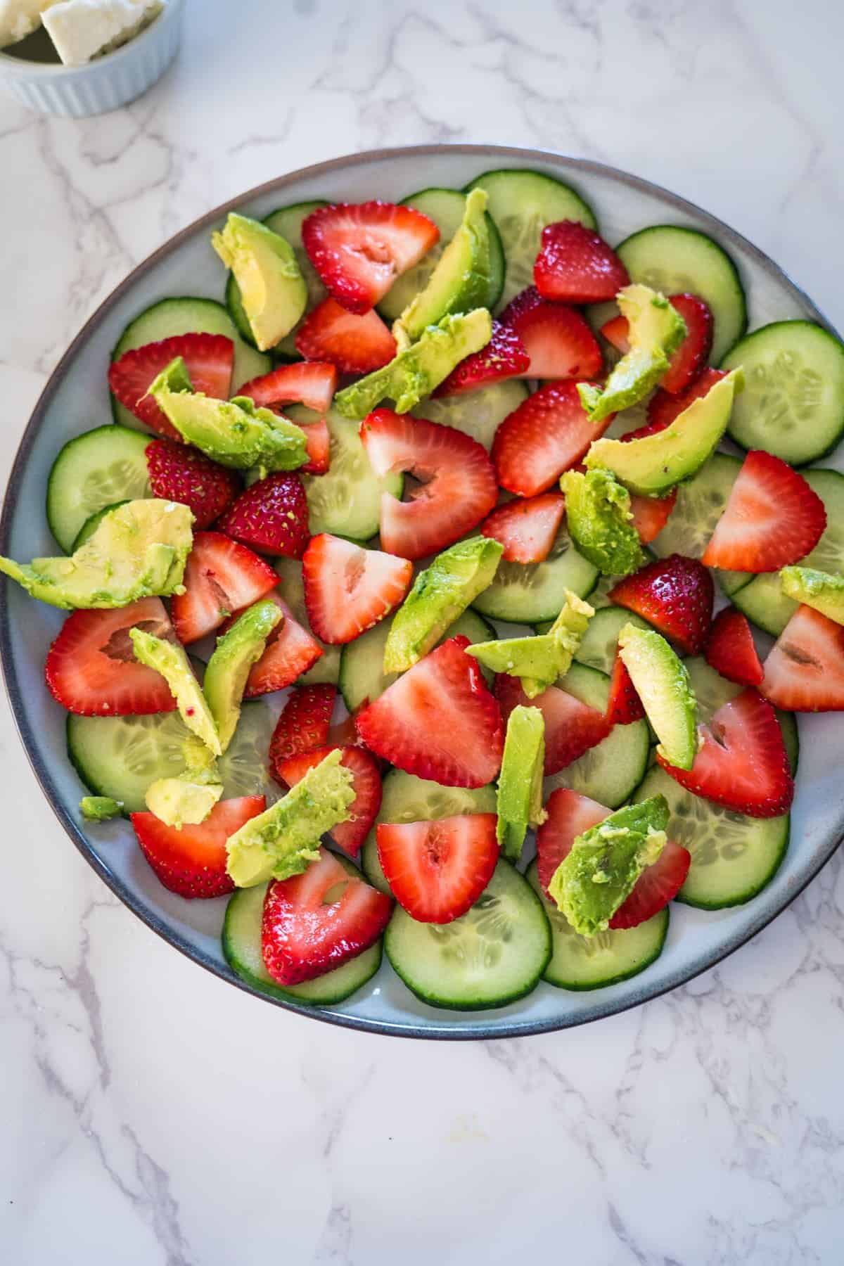 A colorful cucumber and strawberry salad with sliced avocados arranged on a round plate.