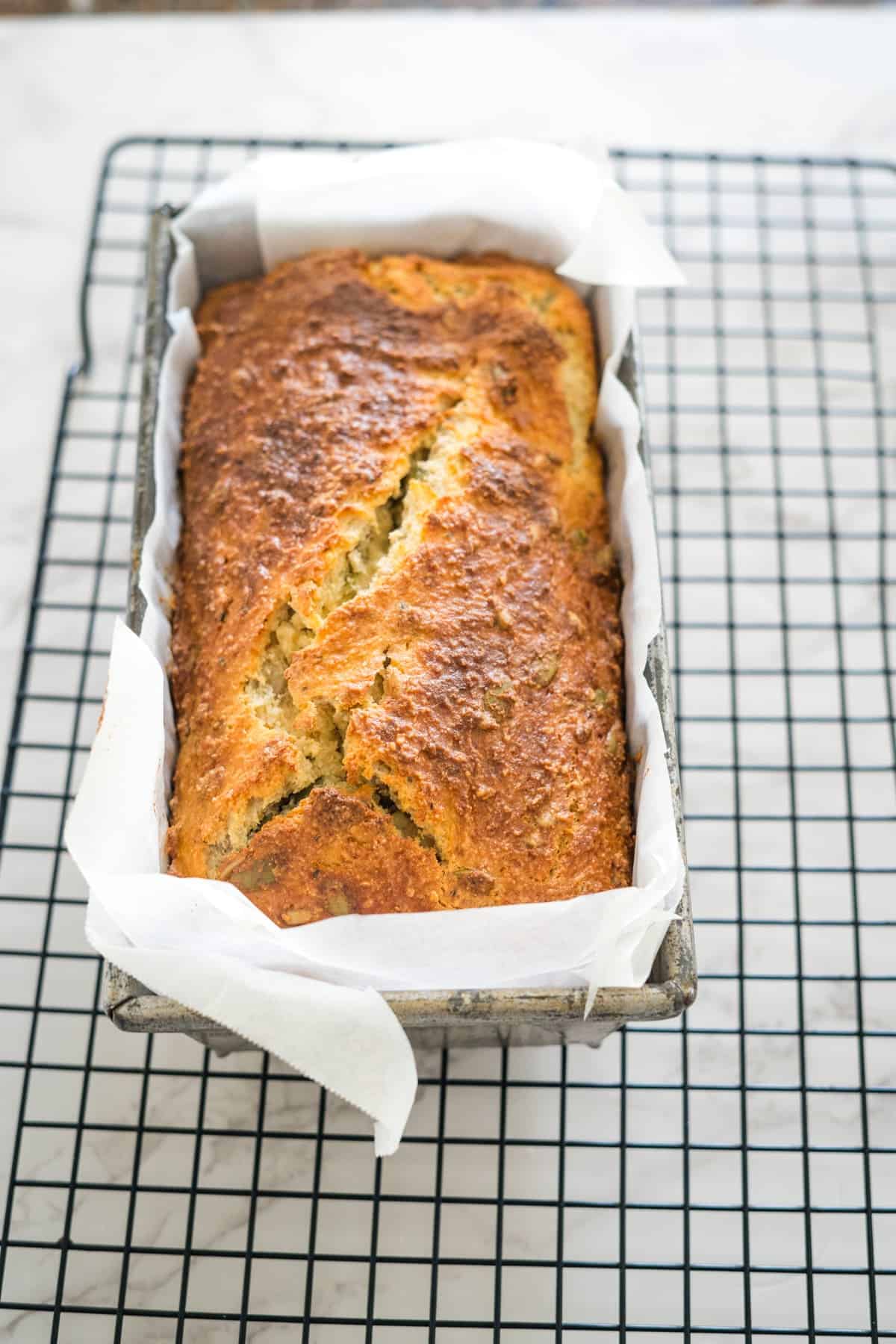 A freshly baked loaf of cottage cheese bread in a parchment paper-lined pan rests on a cooling rack.