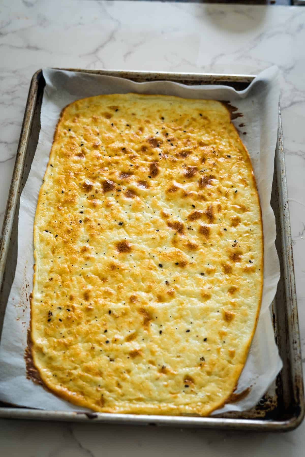 A rectangular piece of baked flatbread with a golden-brown top on a parchment-lined baking sheet.