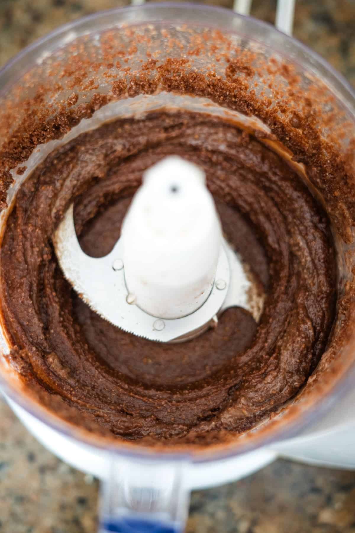 A food processor filled with a smooth, brown mixture, possibly batter or sugar-free Nutella, sits on a countertop.