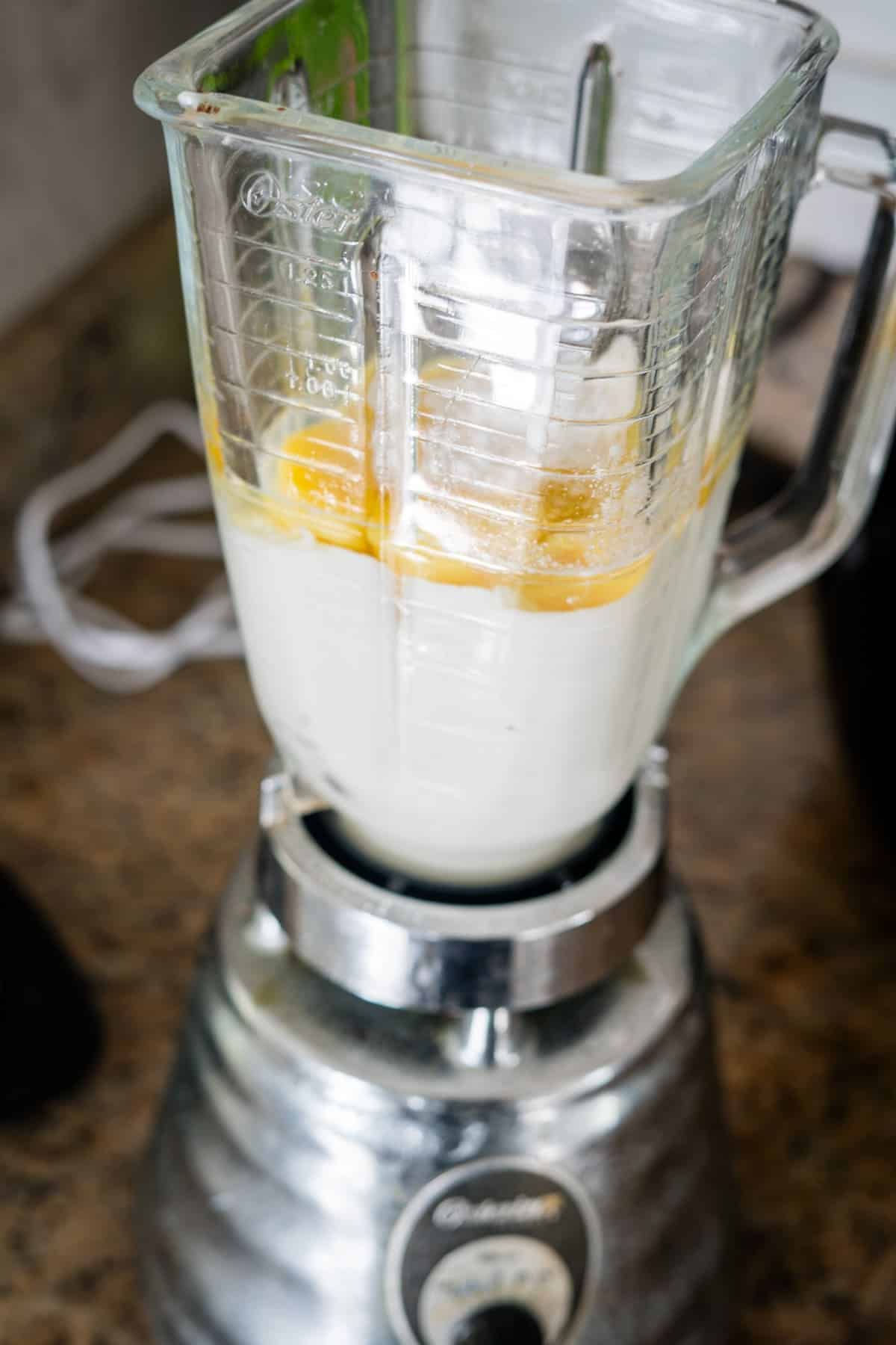 A blender on a kitchen counter containing a mixture of milk and cracked eggs, ready for blending.