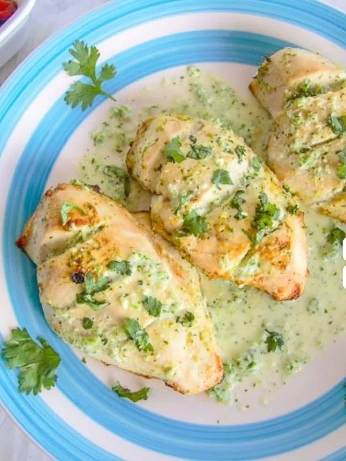 Three grilled chicken breasts garnished with chopped cilantro and creamy green sauce, reminiscent of chicken kofta kebabs, served on a blue-rimmed plate.