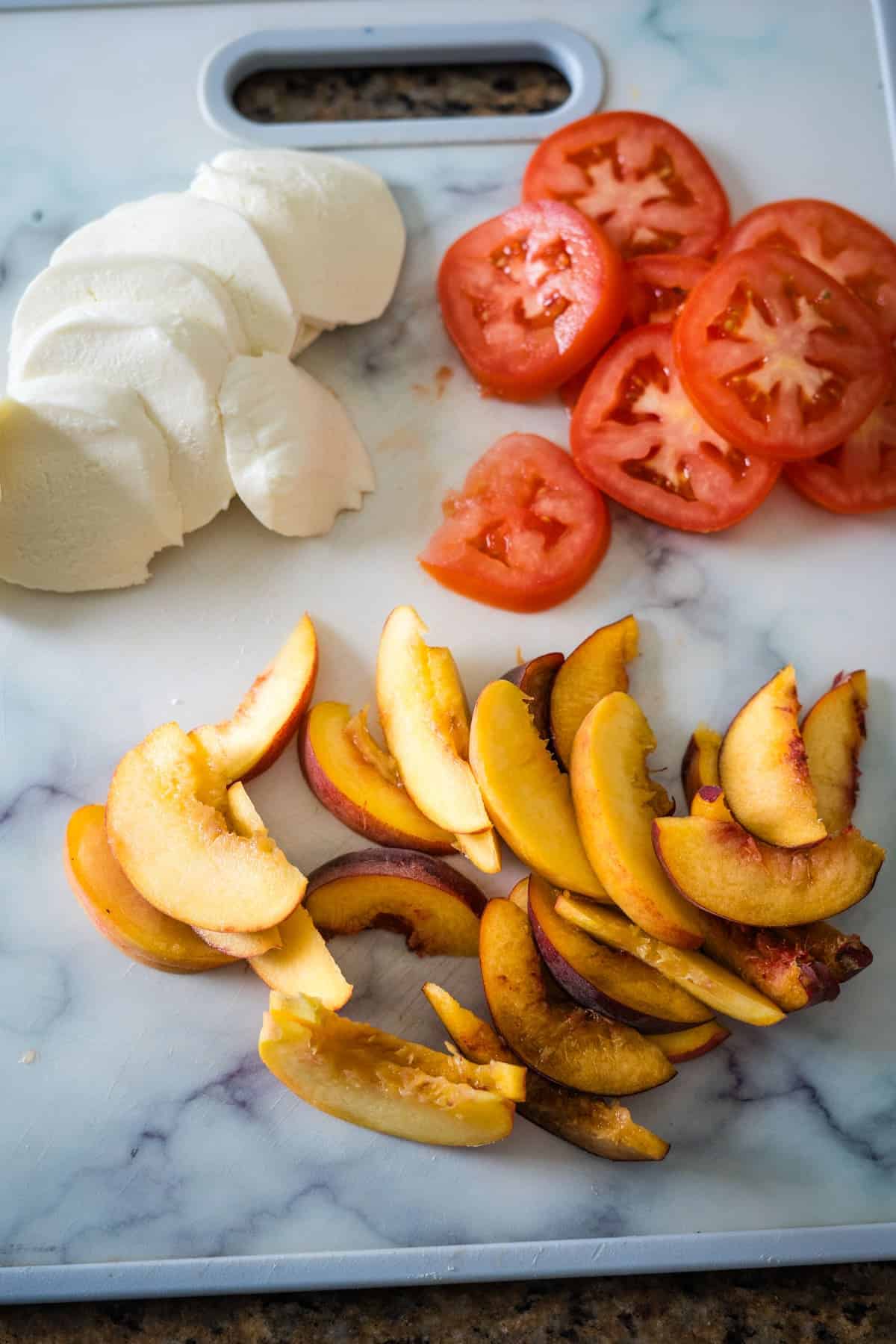 mozzarella, tomatoes and peaches sliced, on a board.