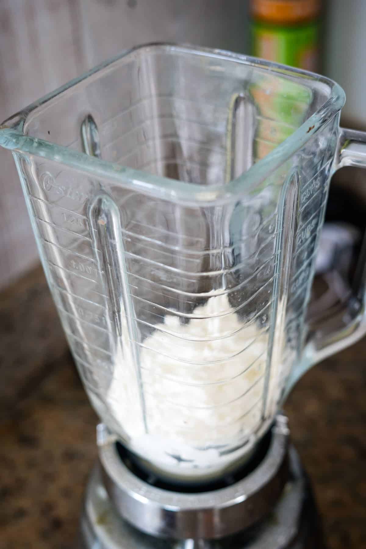 A blender on a kitchen countertop contains a small amount of white powder, ready to mix into creamy cottage cheese for delicious cookies.