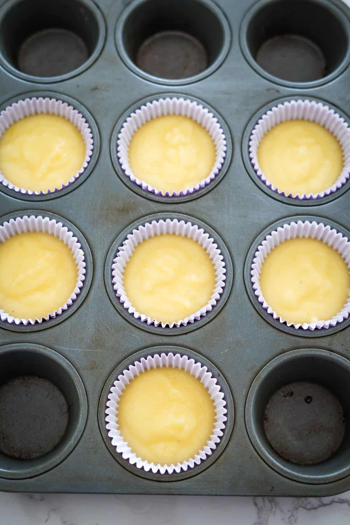 A muffin tin with eight paper liners filled with yellow batter, ready for baking lemon lavender cupcakes.