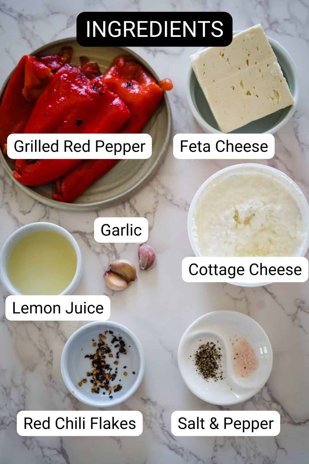 Top-down view of various ingredients on a marble surface including grilled red pepper, feta cheese, cottage cheese, garlic, lemon juice, red chili flakes, and salt and pepper.