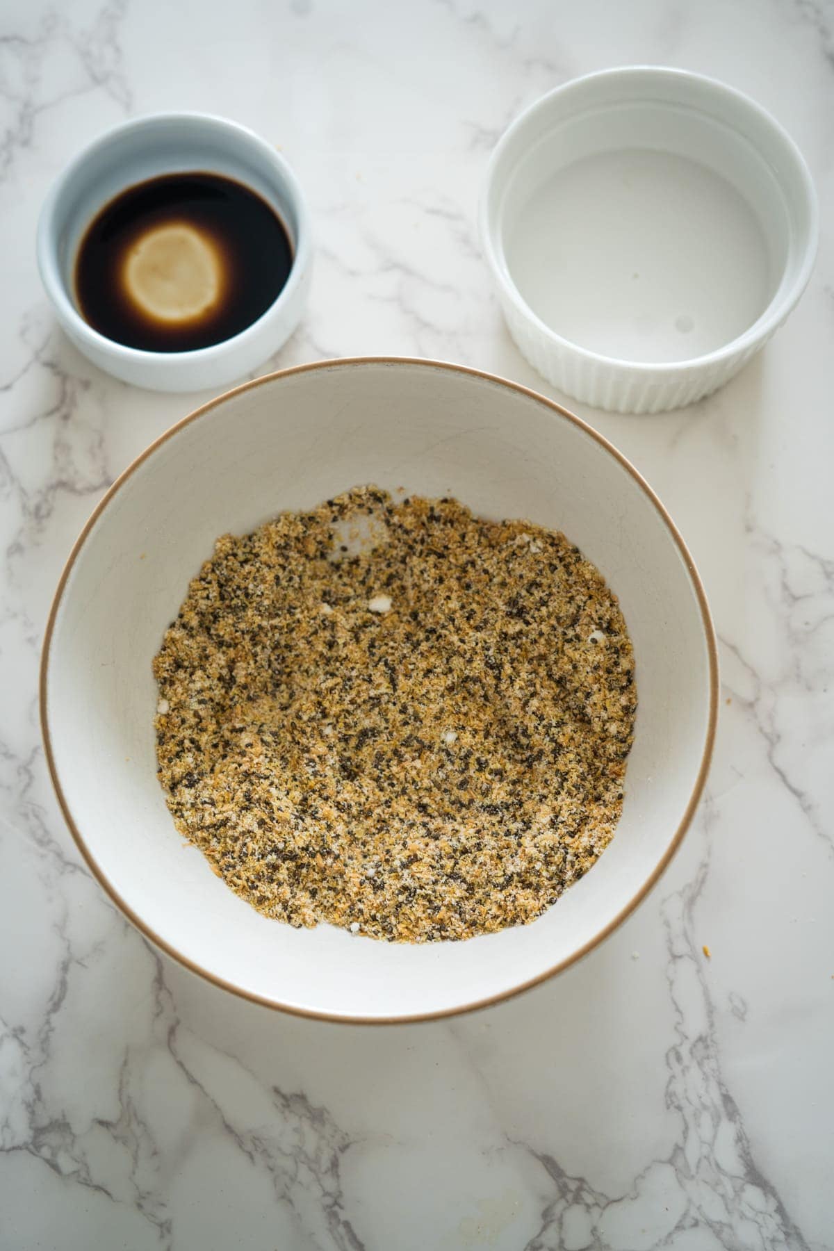 A bowl of chia and flaxseed pudding next to a small bowl of soy sauce and an empty bowl on a marble surface.