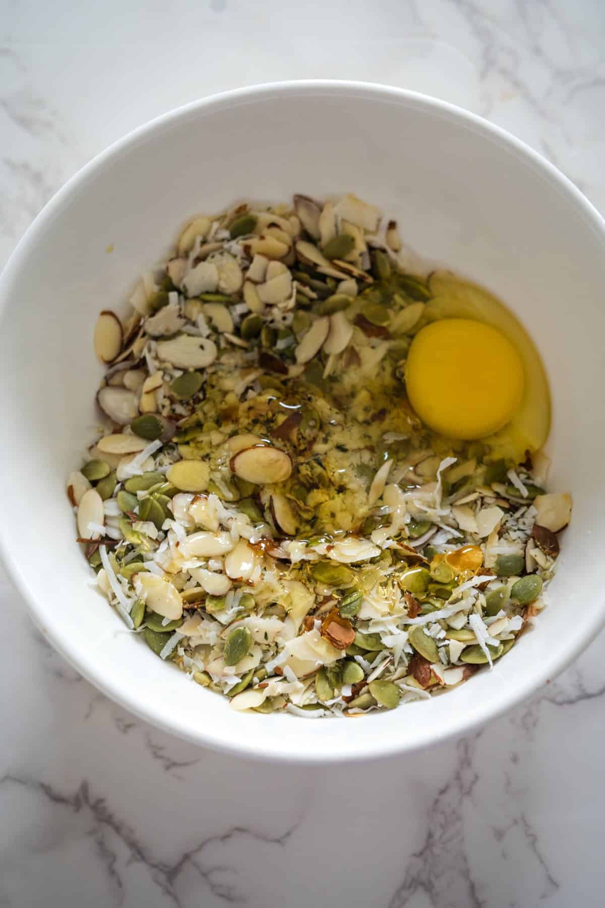 A bowl containing keto breakfast cookies made with an egg, almonds, pumpkin seeds, and spices on a marble surface.