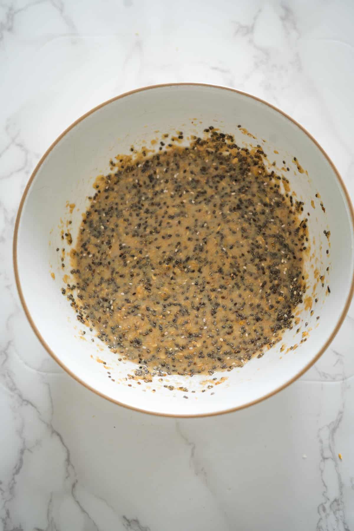 A bowl containing freshly mixed chia and flaxseed pudding on a marble surface.