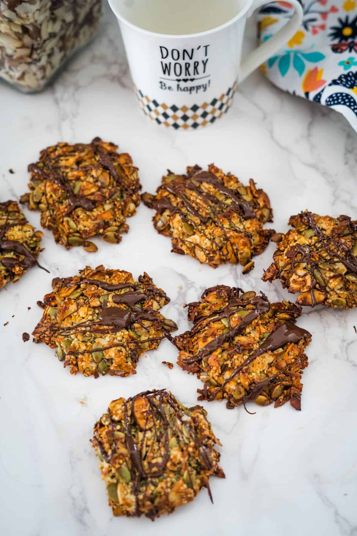 Homemade keto granola bars with chocolate drizzle on a marble countertop, next to a mug with the text "Don't worry, be happy!