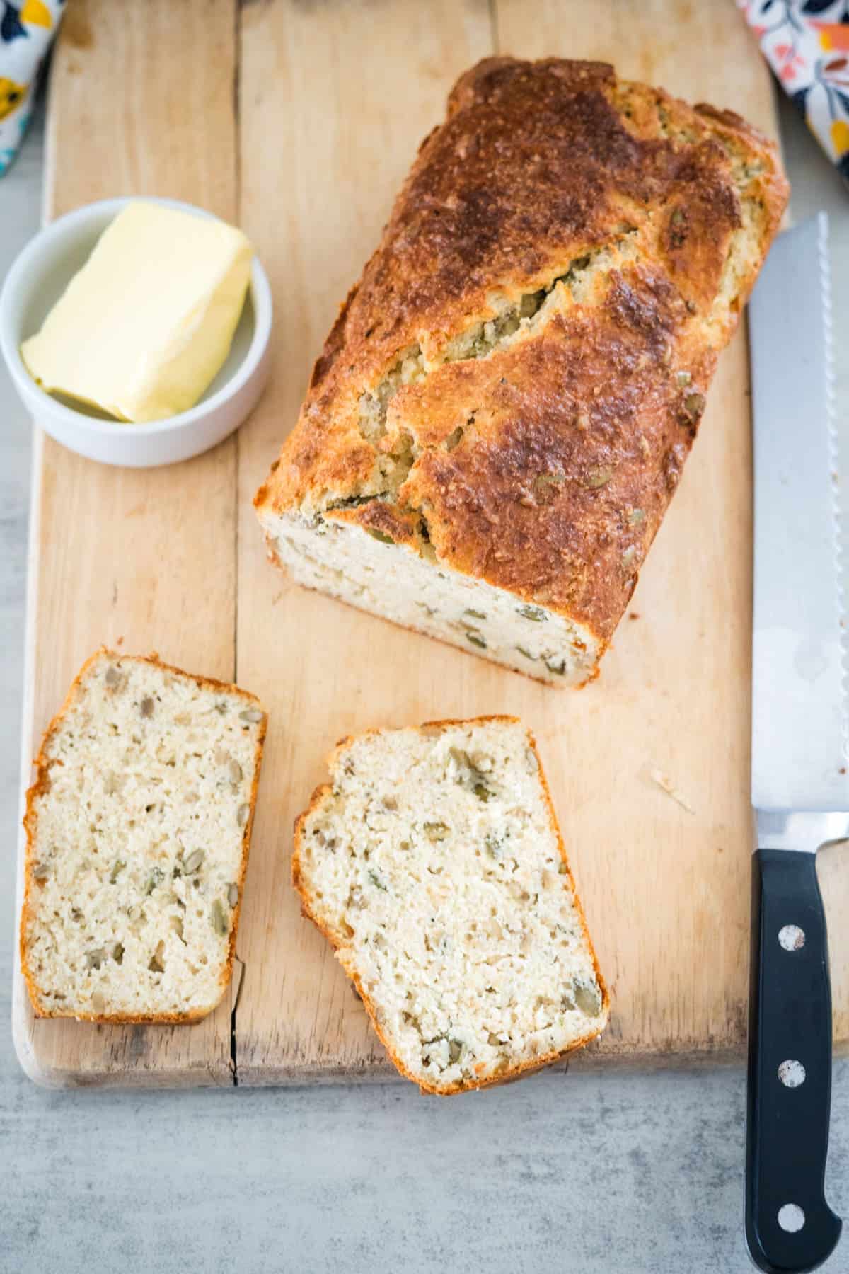 A loaf of cottage cheese bread with two slices cut, placed on a wooden cutting board with a knife and a dish of butter.