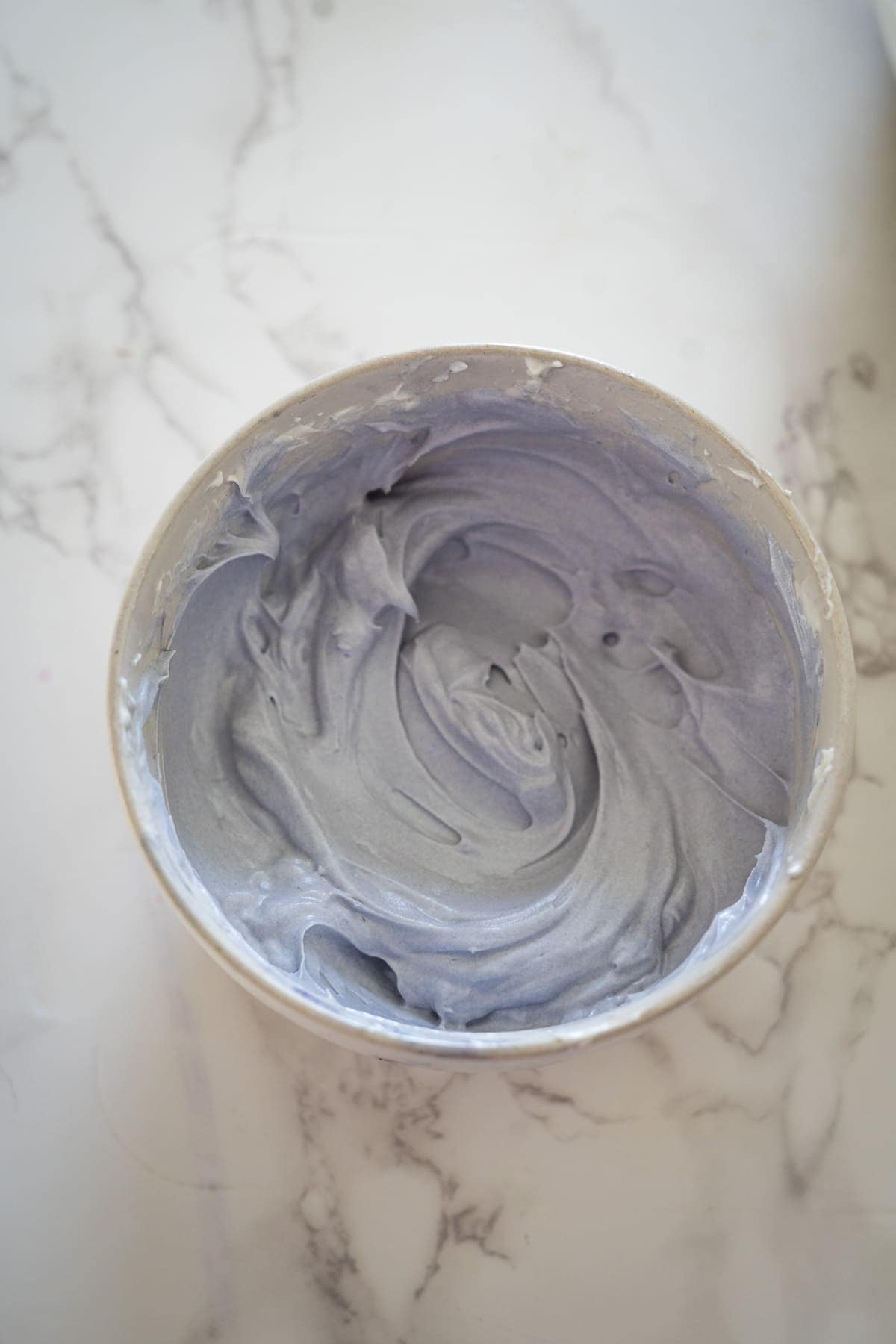 A bowl containing a creamy, purple mixture that hints at the delightful flavors of lemon lavender cupcakes rests on a marble countertop.