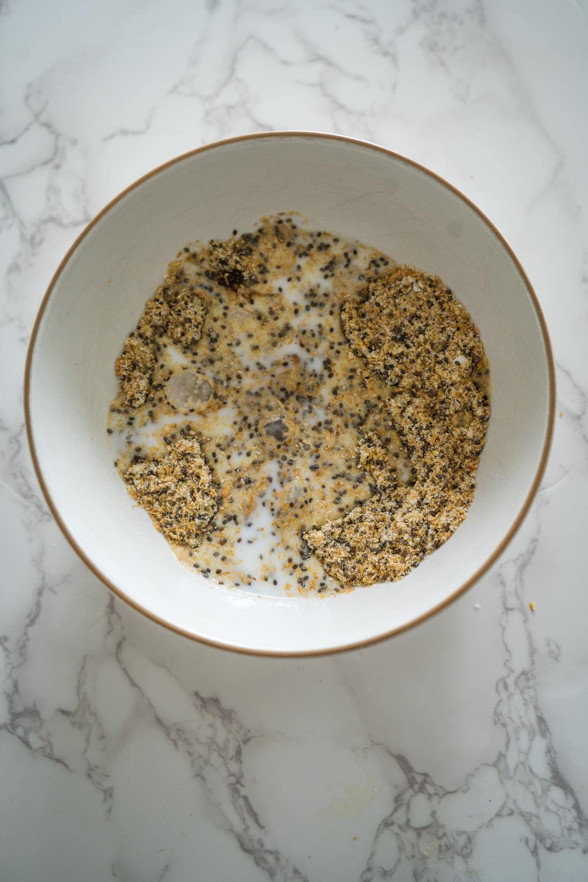 A bowl of chia and flaxseed pudding with milk on a marble surface.