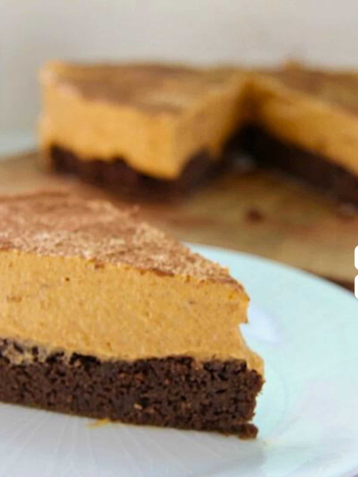 A slice of layered dessert with a thick brown base and creamy orange topping, set on a white plate, with another slice in the background.