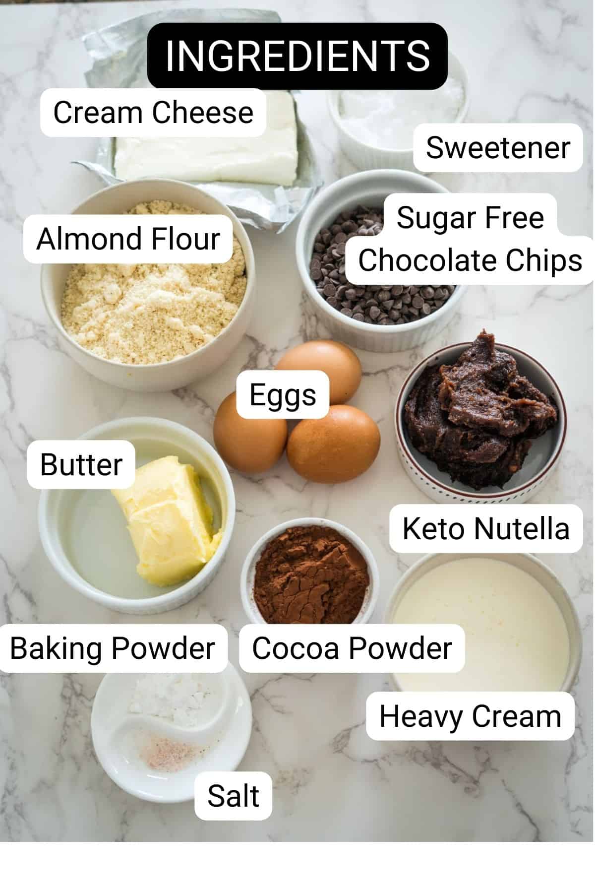 Ingredients on a marble surface include cream cheese, sweetener, almond flour, sugar-free chocolate chips, eggs, butter, keto Nutella, baking powder, cocoa powder, heavy cream, and salt—perfect for creating a luscious Nutella brownie cheesecake.