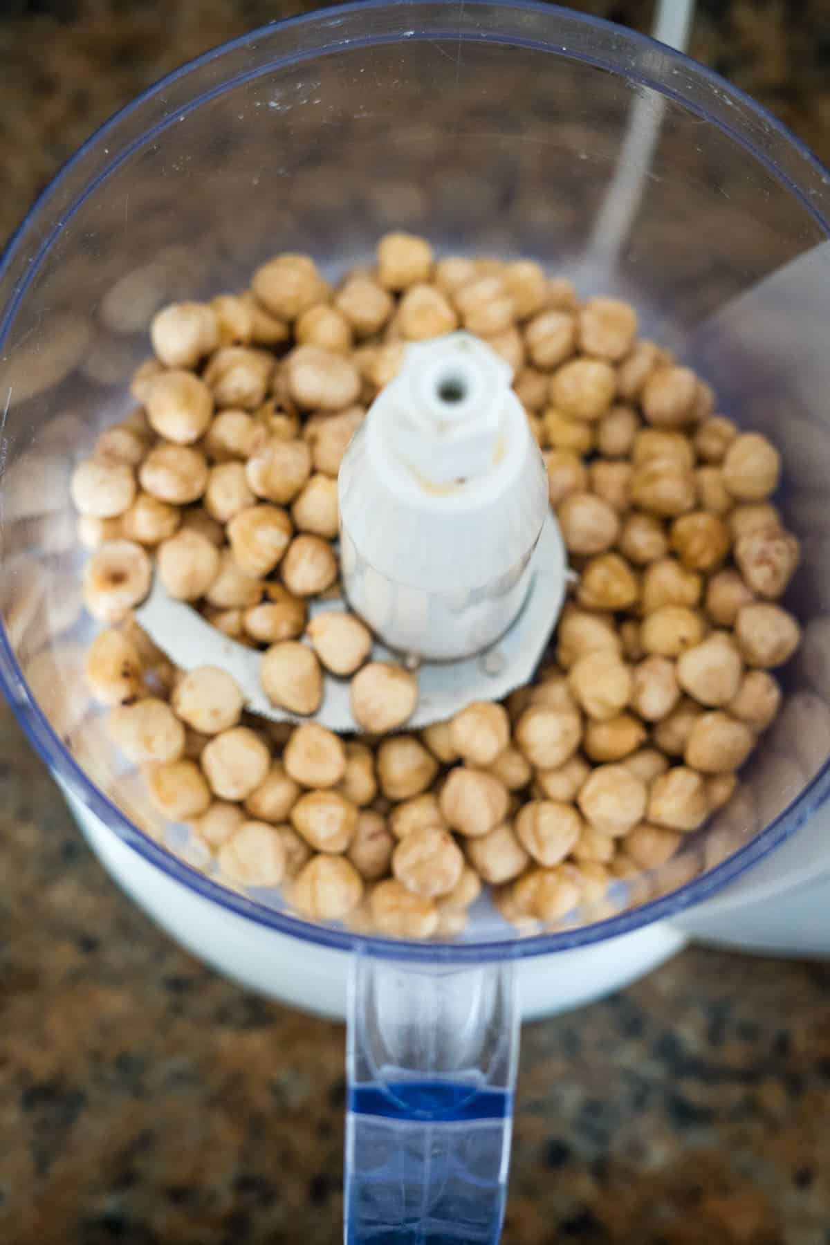 A food processor bowl filled with chickpeas, placed on a countertop, ready to be blended into a delicious, sugar-free Nutella spread.