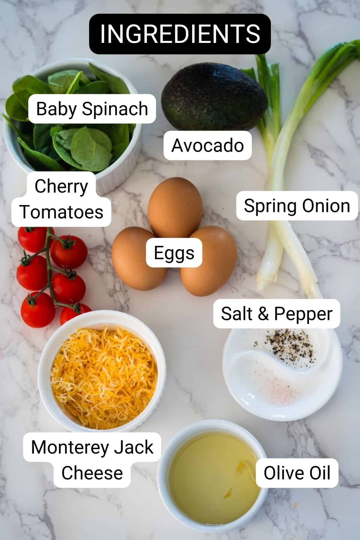 An organized layout of fresh ingredients including baby spinach, avocado, cherry tomatoes, spring onion, eggs, shredded cheese, salt and pepper, and olive oil on a marble surface.