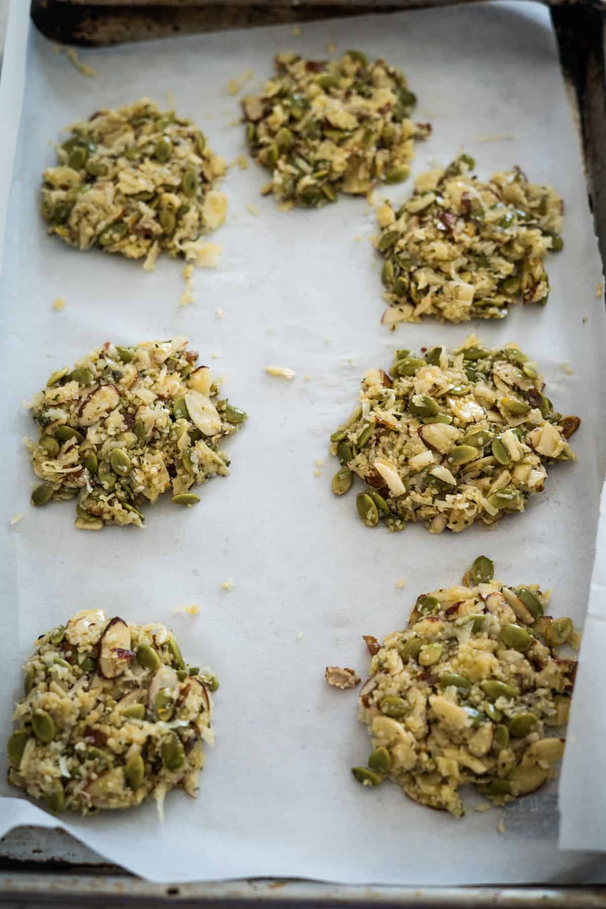 Six keto vegan cookies made of seeds and nuts arranged on parchment paper on a baking tray.