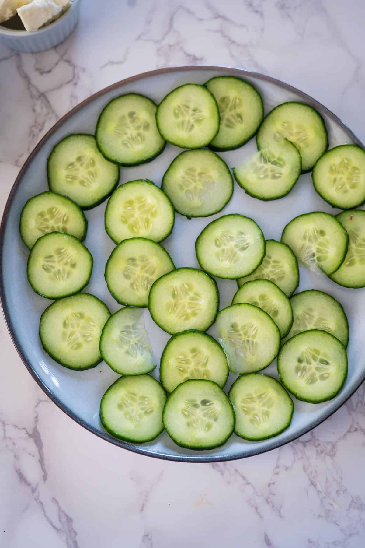 Sliced cucumbers and strawberries neatly arranged on a blue plate, viewed from above, with a small bowl of dip in the background.