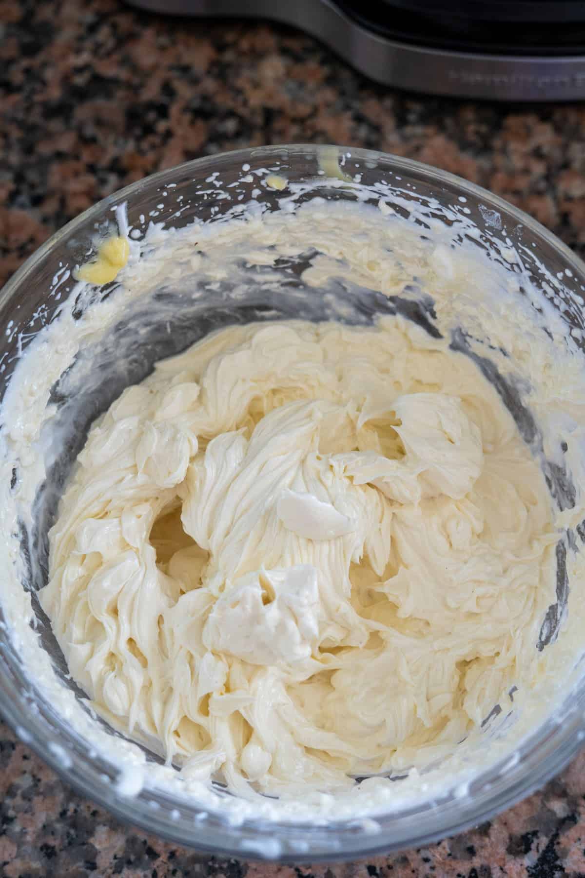 A glass bowl filled with whipped cream sits on a granite countertop, ready to be paired with freshly baked lemon lavender cupcakes.