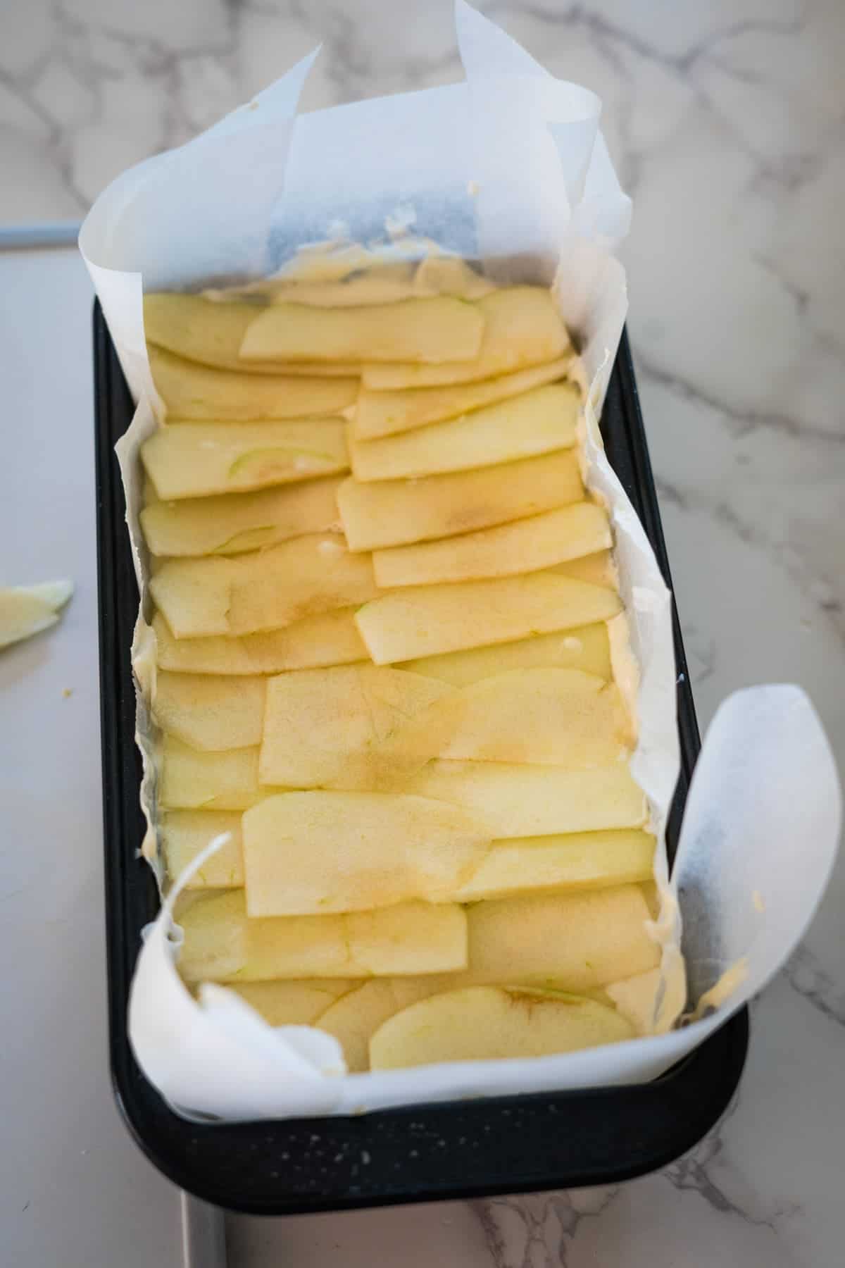 A baking pan lined with parchment paper and filled with neatly arranged thin apple slices, ready to be baked.