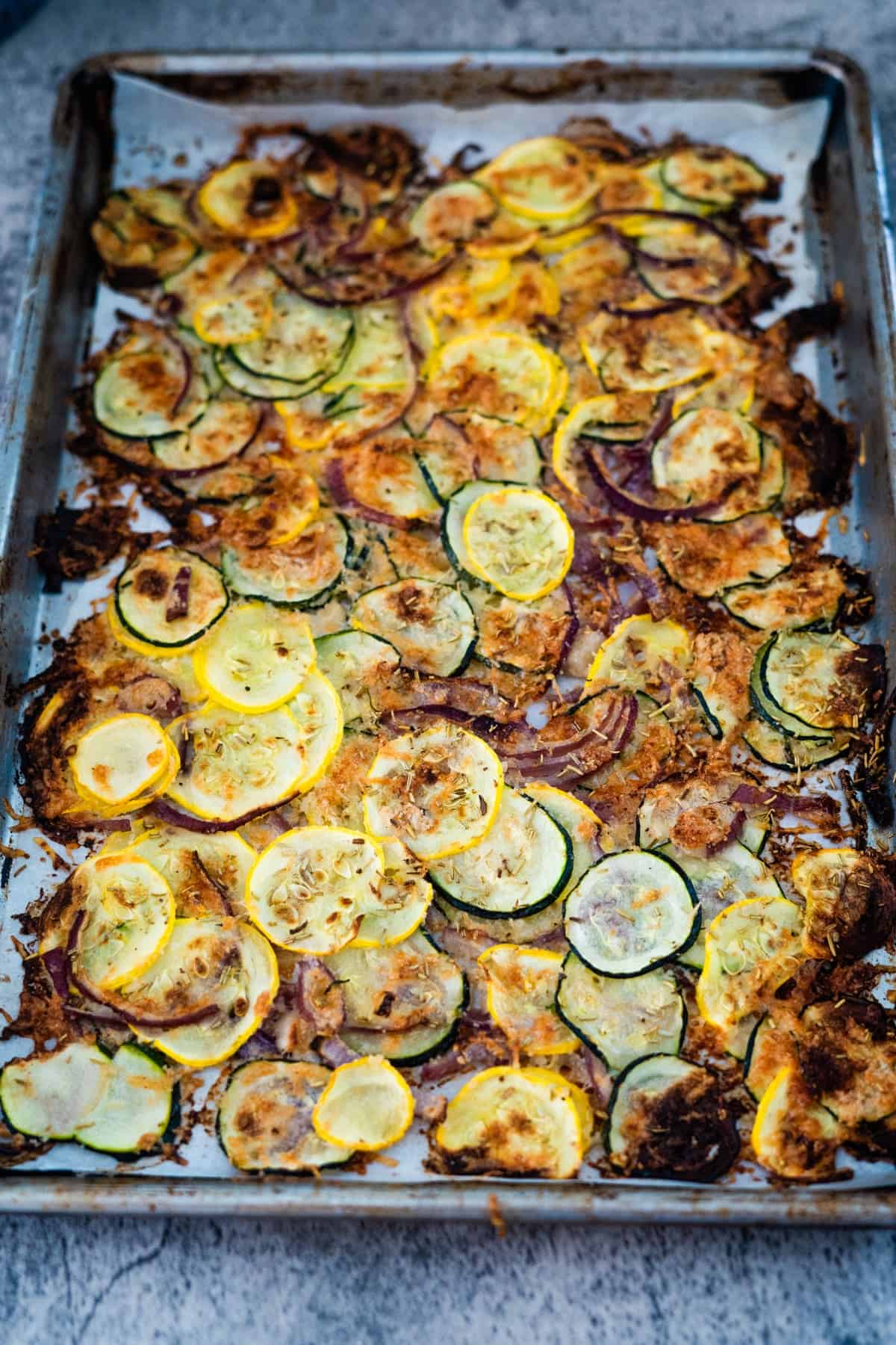 A baking sheet filled with roasted slices of yellow and green zucchini, topped with melted cheese and browned to a crisp.