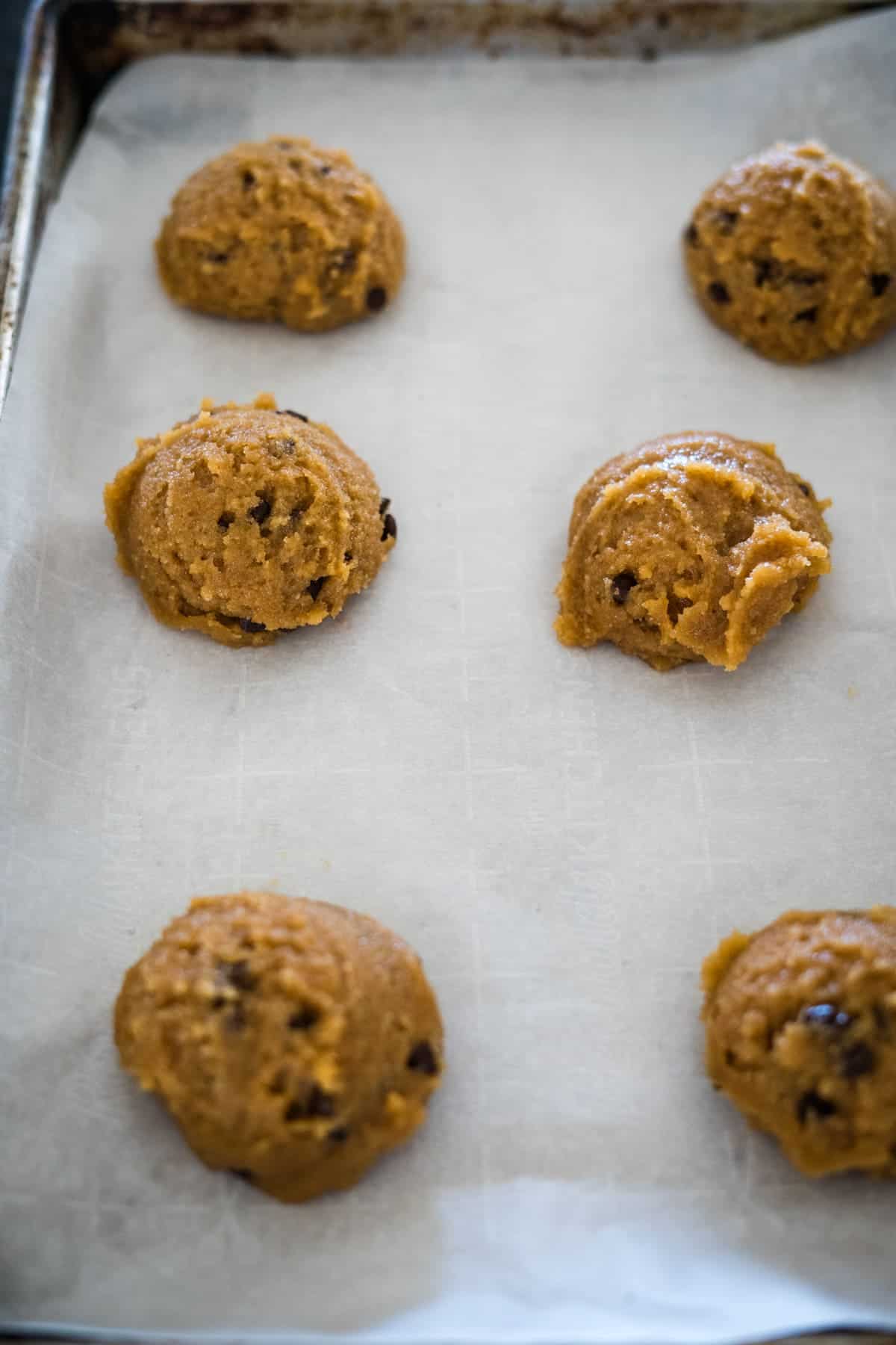 Unbaked cookie dough balls placed on a parchment-lined baking sheet.