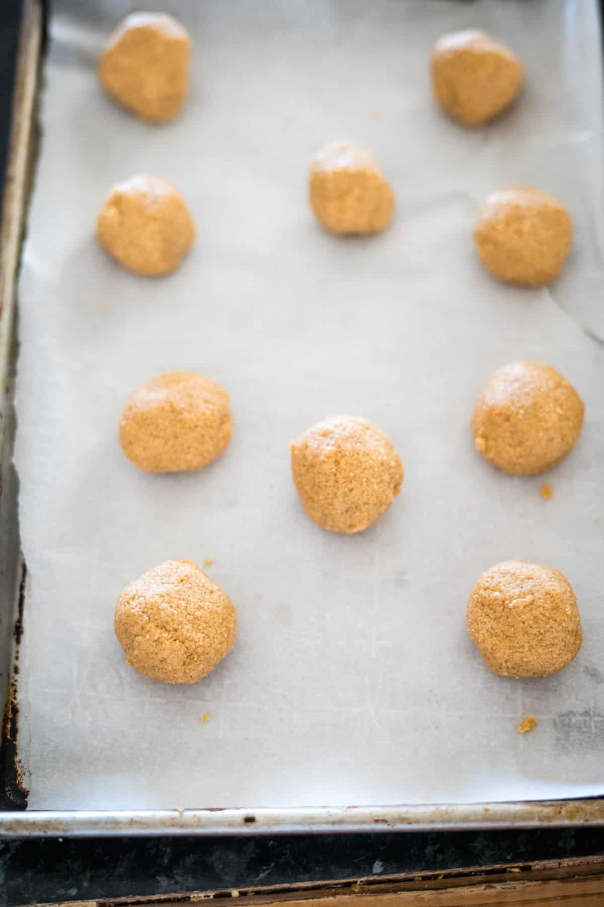 A baking tray with balls of unbaked cookie dough placed on parchment paper, ready for the oven.