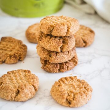 A stack of five peanut butter cookies is surrounded by four individually placed cookies on a marble countertop.