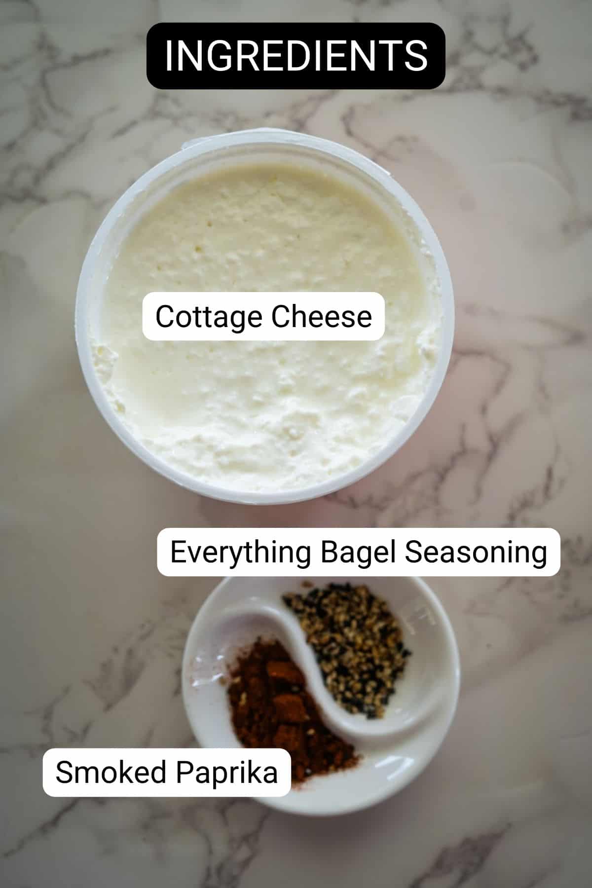 A container of cottage cheese, a small dish with everything bagel seasoning, and a small dish with smoked paprika labeled as ingredients.