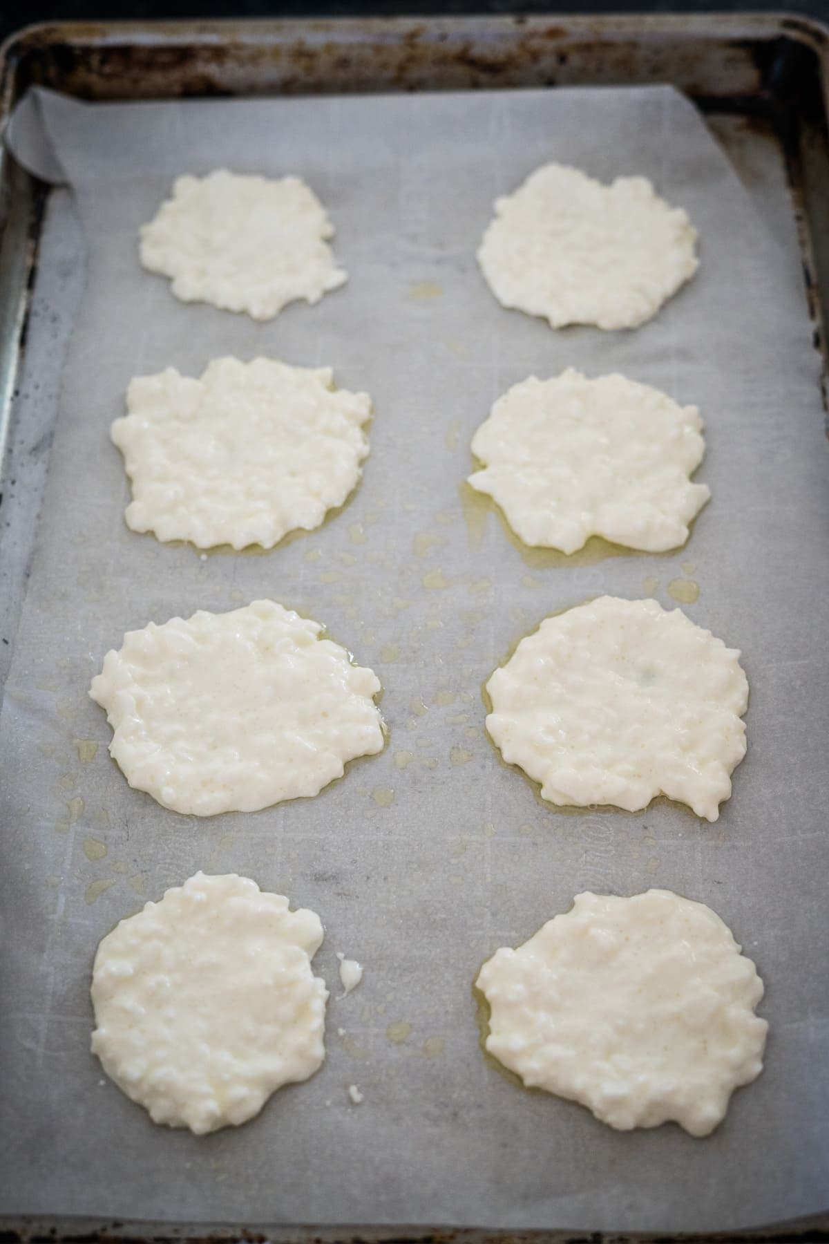 A baking sheet is lined with parchment paper and topped with eight dollops of uncooked cottage cheese.