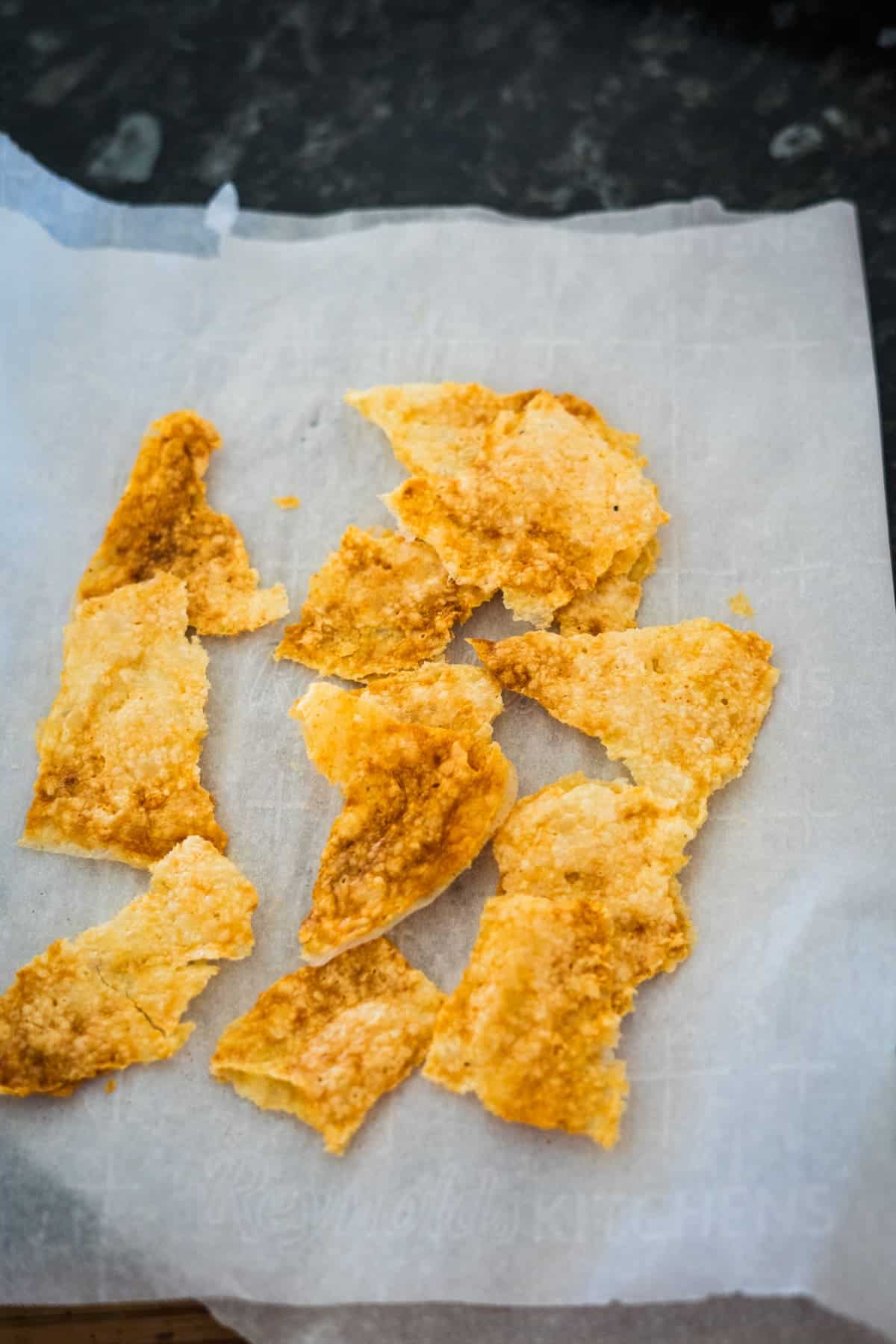 Golden brown cheese crisps on a sheet of parchment paper.