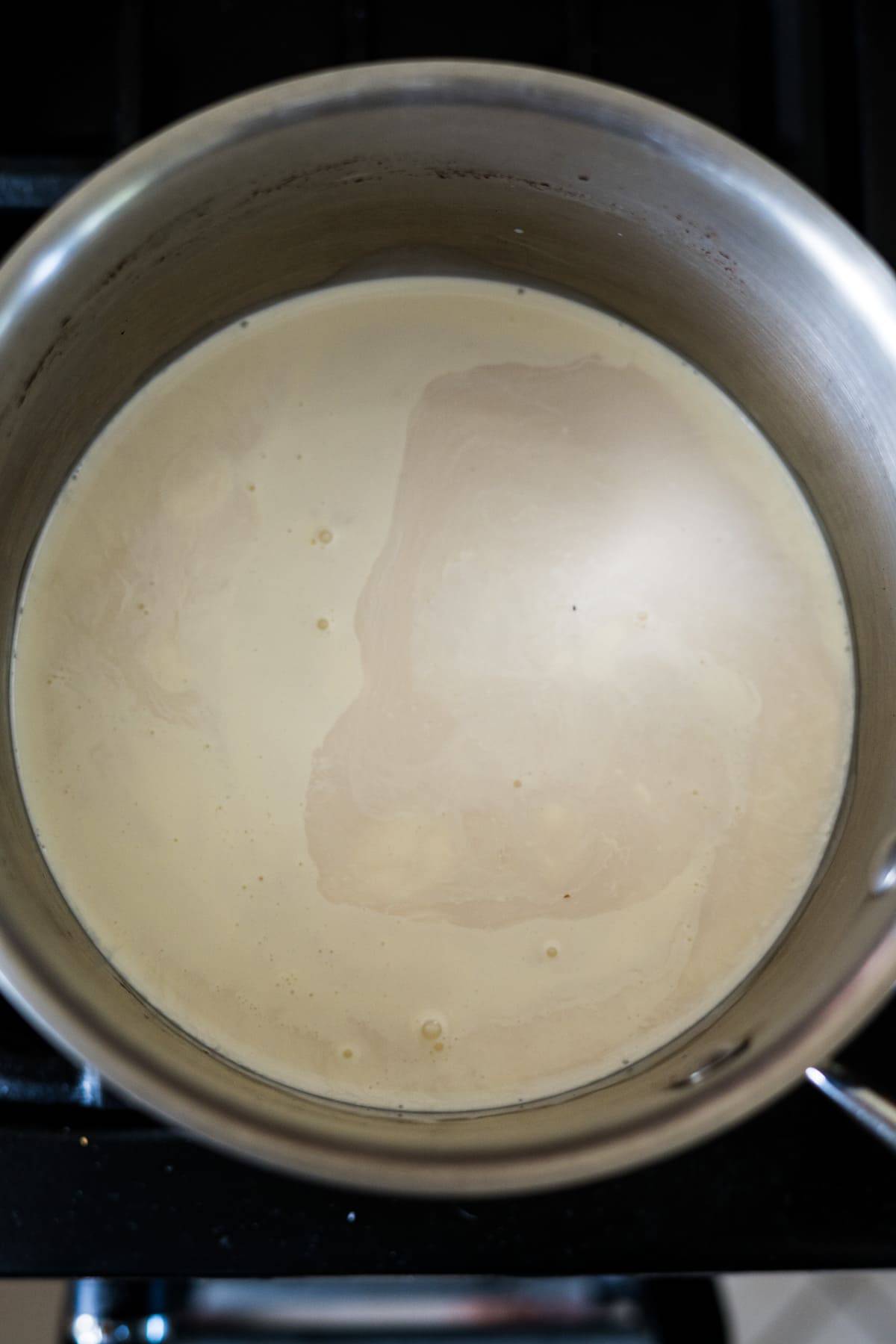 A pot filled with simmering milk on a stovetop, the beginnings of keto vanilla ice cream. The milk shows a thin layer on its surface.