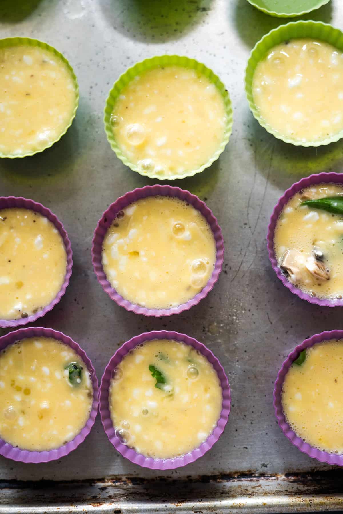 Silicone muffin molds filled with a cottage cheese egg mixture are placed on a metal baking sheet, ready for baking.