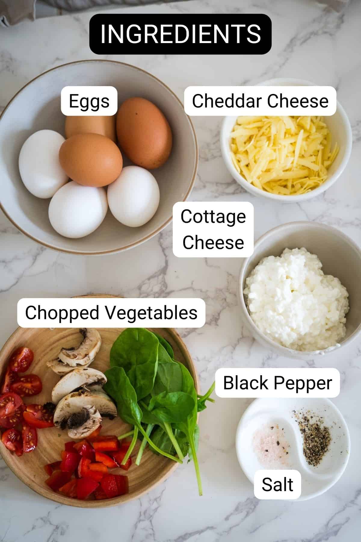 Ingredients for delicious cottage cheese egg muffins displayed on a marble countertop: eggs, shredded cheddar cheese, cottage cheese, chopped vegetables (tomatoes, mushrooms, spinach, red bell pepper), black pepper, and salt.